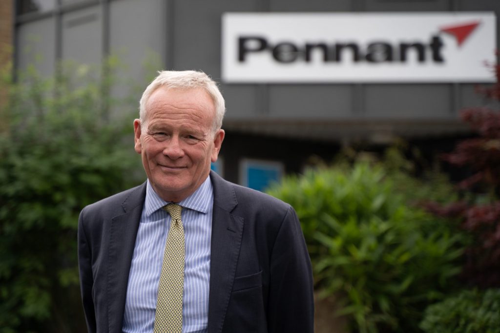 A picture of a person in front of a building with the word Pennant on. They are wearing a suite with a yellow tie.