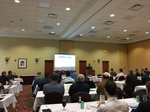 A conference room full of people sat in rows at tables listening to a presentation