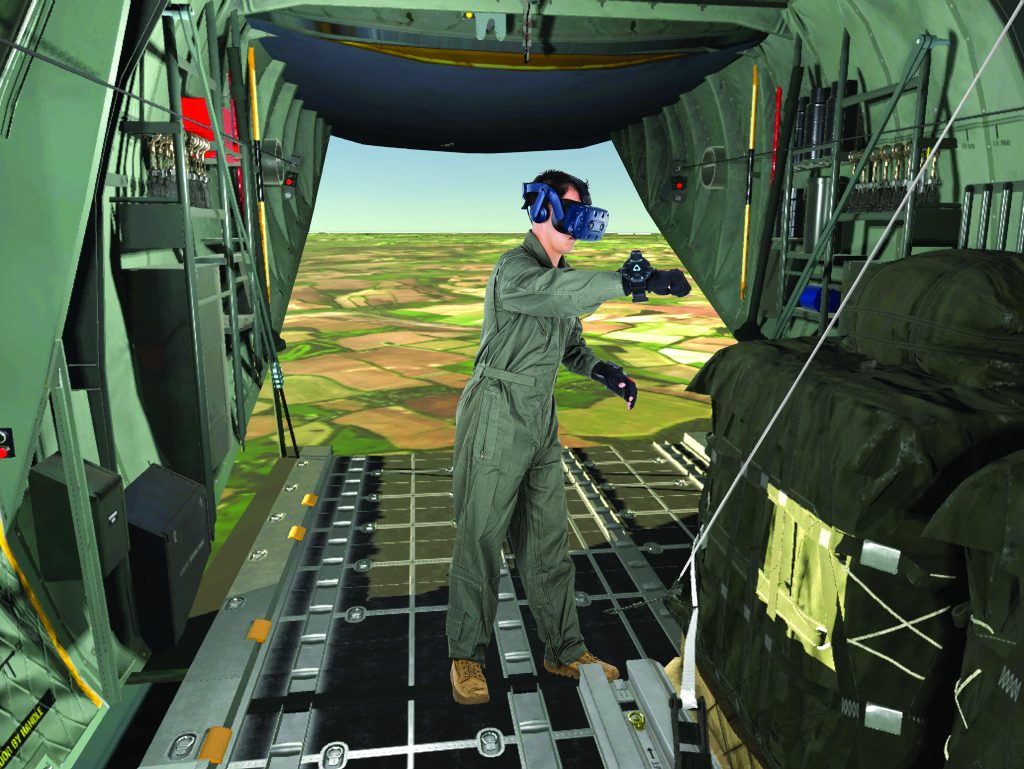 A person in a flight suit and VR headset stands inside the open cargo bay of a military aircraft, seemingly interacting with a virtual environment that includes green landscapes.