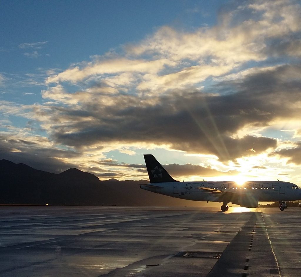 An airport runway. The sky is blue with the sun setting over an aeroplane