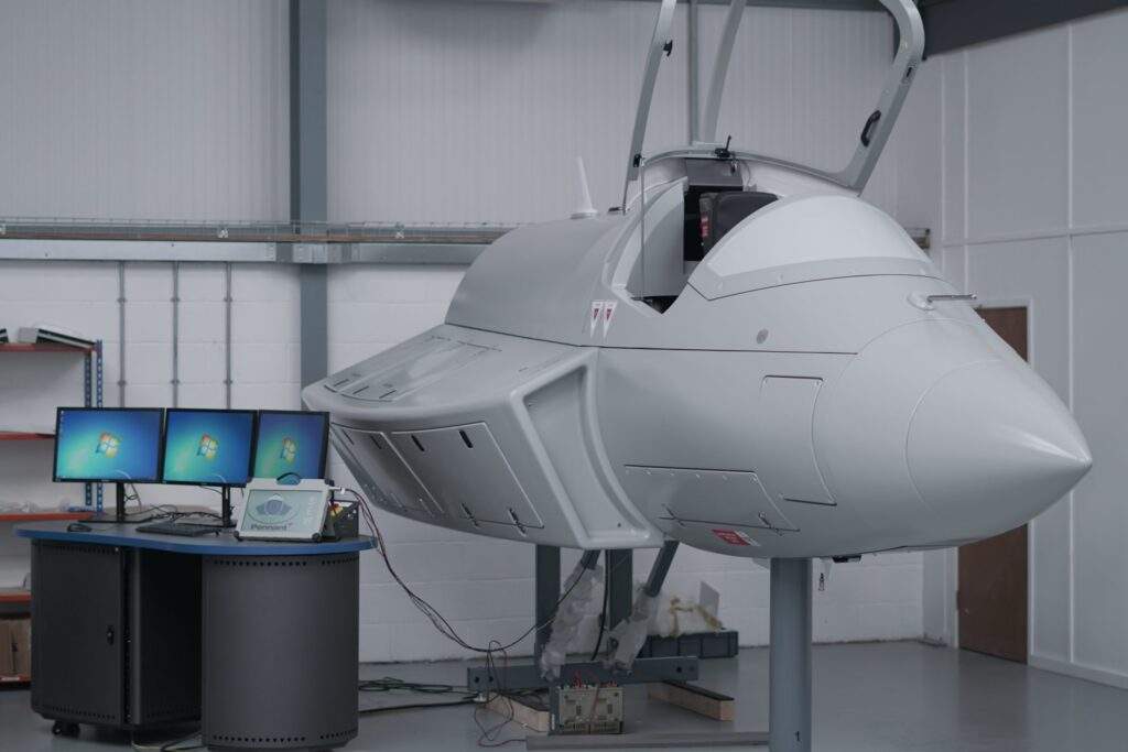 PENNANT SUPPORT NEXTGEN RAAF TRAINING 19 Two large grey hardware training devices. The device have multiple panels open and documentation on a stand in front of it
