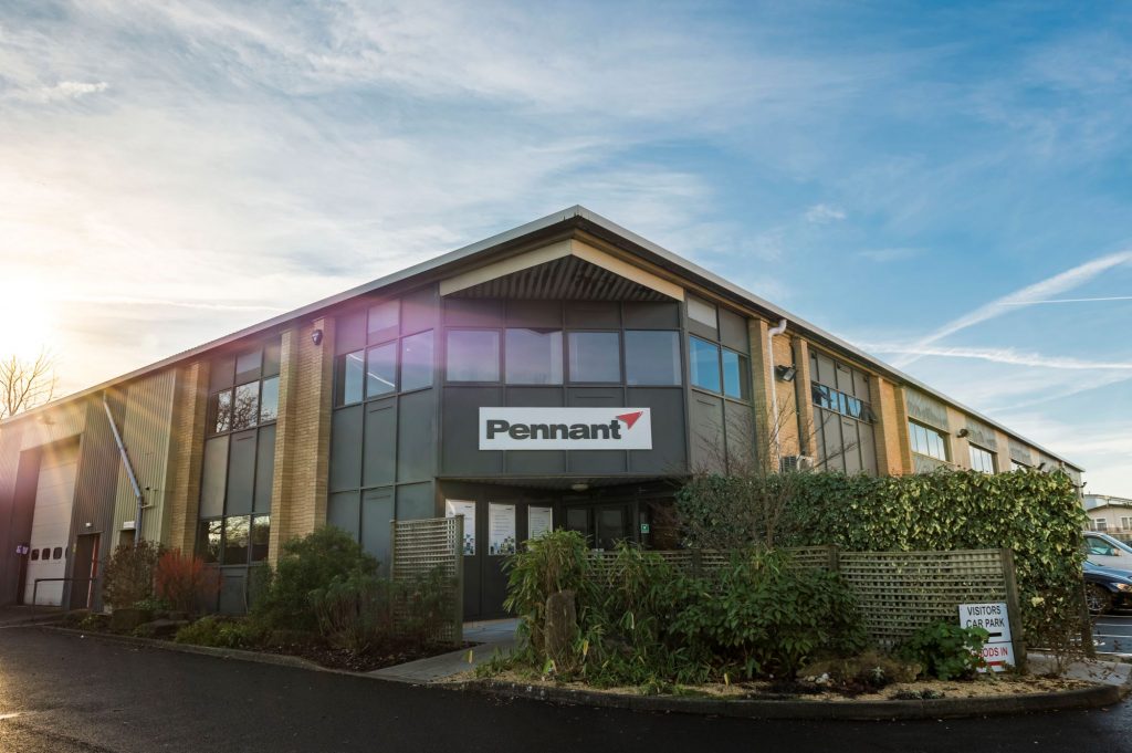 A large office building with a sign that says Pennant on it. The background is sky blue and green hedges.