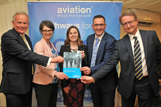 A group of five people stood together smiling. They are all wearing suites