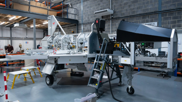 A modern manufacturing facility with complex machinery, including a large mechanical apparatus with various components and a control panel, set up for assembly or testing processes