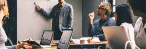 PART 2: “IMPLEMENTING AN S1000D PROJECT – WHAT YOU ABSOLUTELY NEED TO KNOW!” 11 A group of smartly dressed professional sat around a table looking at someone pointing to a whiteboard. They are smiling and all sat with open laptops