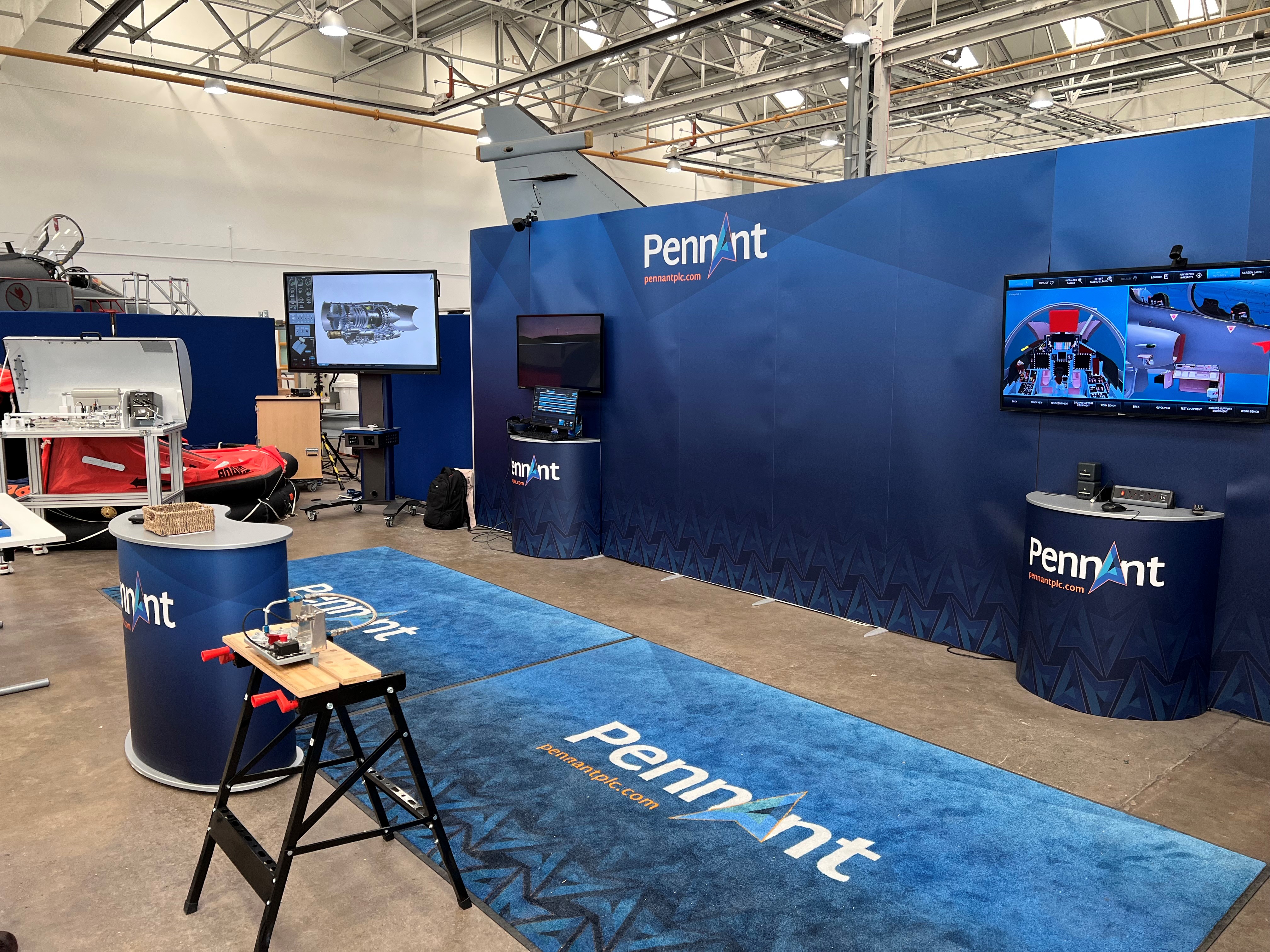An image of what appears to be an exhibition stand. The stand backdrop is dark navy and there is a variety of equipment and products on display including screens, and hardware engineering equipment.