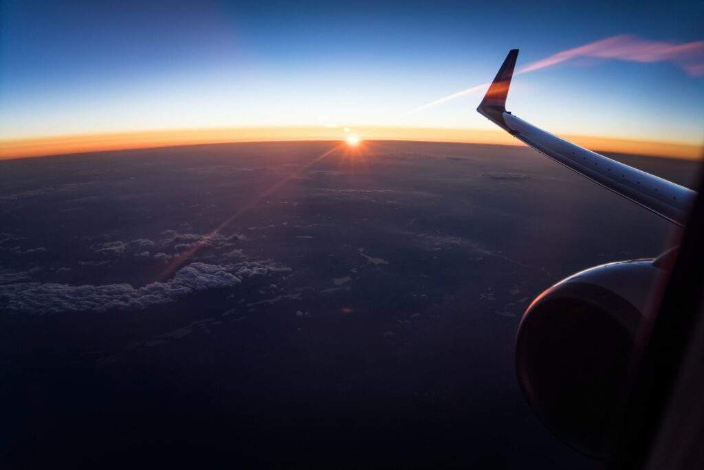 Our Head of IPS & Strategic Development is at the launch of the UK Chapter of CLEP 31 A breathtaking view from an airplane window during sunset, where the sun casts a warm glow against the darkening sky, illuminating the clouds and earth below.