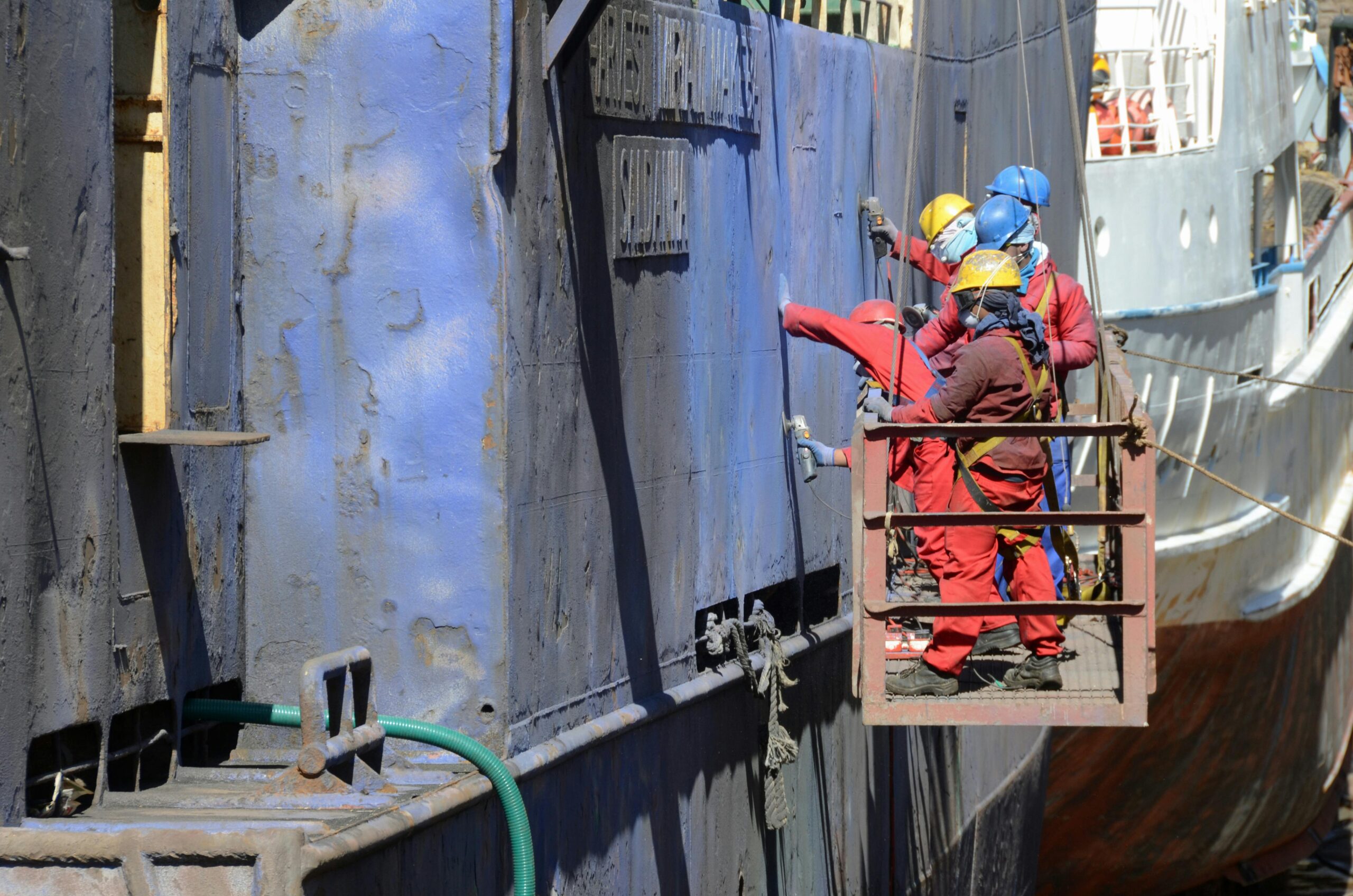 engineers in orange work uniform working on the side of a ship